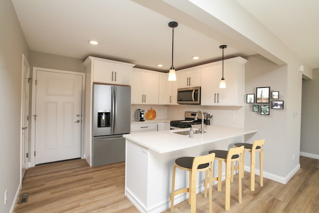 kitchen featuring appliances with stainless steel finishes, light hardwood / wood-style floors, white cabinets, kitchen peninsula, and pendant lighting