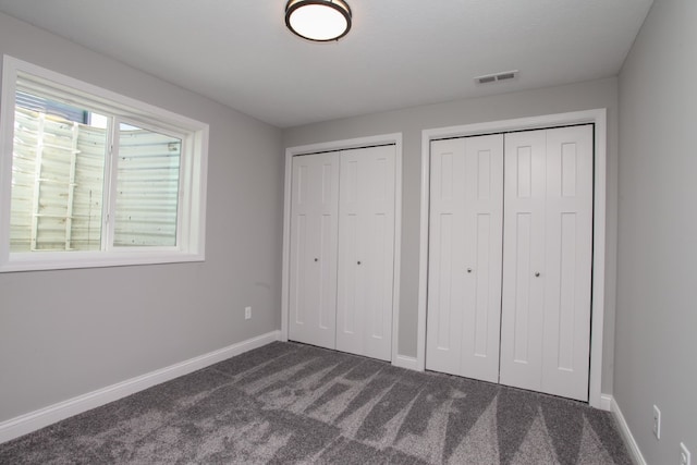 unfurnished bedroom with multiple closets and dark carpet