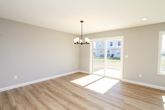 unfurnished room featuring an inviting chandelier, light hardwood / wood-style floors, and a wealth of natural light