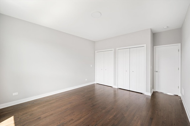 unfurnished bedroom featuring dark hardwood / wood-style floors and multiple closets