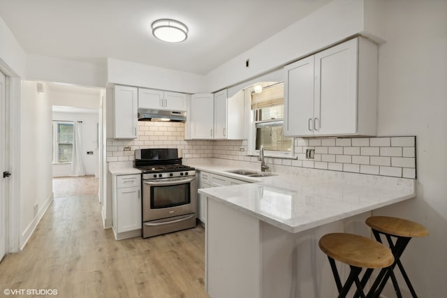 kitchen with a kitchen bar, sink, white cabinetry, light hardwood / wood-style floors, and stainless steel gas range