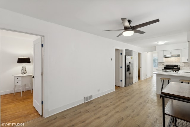 kitchen with decorative backsplash, stainless steel fridge with ice dispenser, light wood-type flooring, ceiling fan, and range