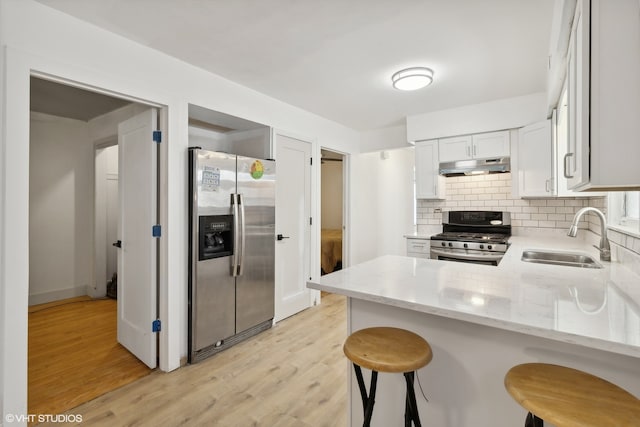 kitchen with decorative backsplash, appliances with stainless steel finishes, kitchen peninsula, light hardwood / wood-style floors, and sink