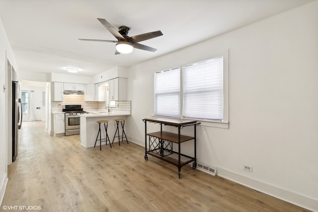 kitchen with light wood-type flooring, stainless steel appliances, a kitchen bar, and kitchen peninsula