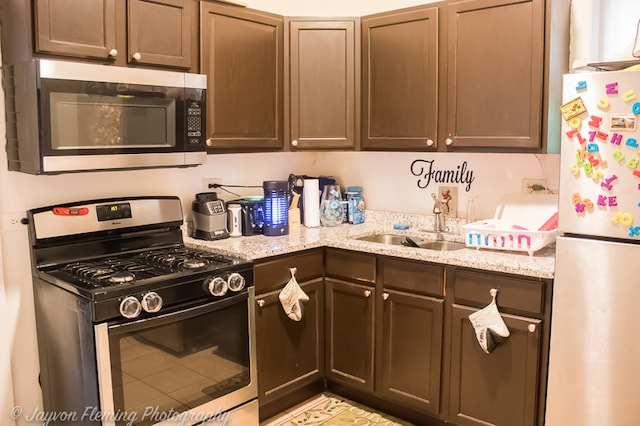 kitchen featuring dark brown cabinets, sink, light stone counters, and stainless steel appliances