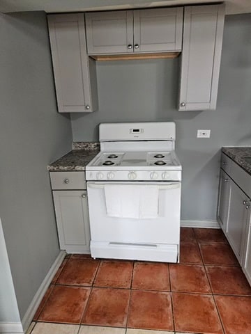 kitchen featuring gray cabinetry, white stove, dark stone countertops, and dark tile flooring