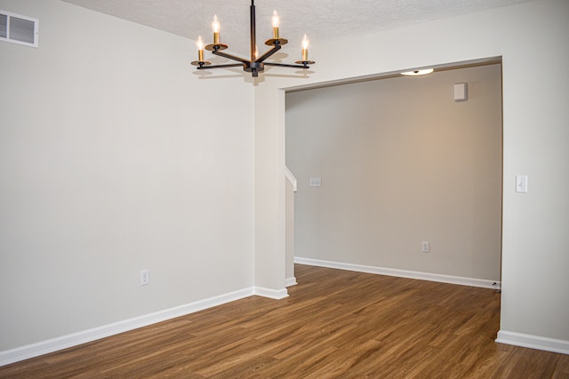 empty room with a textured ceiling, dark hardwood / wood-style floors, and a chandelier