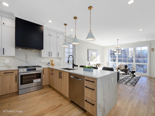 kitchen featuring hanging light fixtures, light stone counters, stainless steel appliances, sink, and white cabinetry