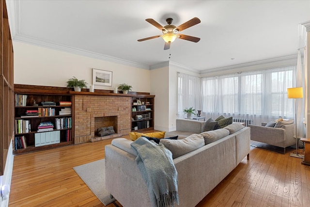 living room featuring a brick fireplace, crown molding, light wood-type flooring, and ceiling fan