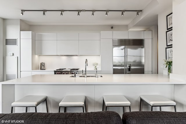 kitchen featuring built in refrigerator, sink, white cabinets, and a breakfast bar area