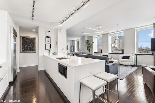 kitchen featuring stainless steel microwave, track lighting, dark wood-type flooring, sink, and white cabinetry