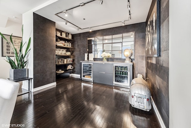 bar featuring beverage cooler, dark wood-type flooring, and rail lighting