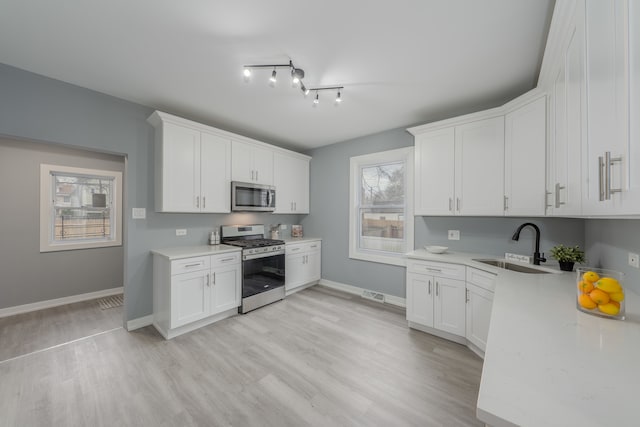 kitchen with white cabinets, stainless steel appliances, light hardwood / wood-style flooring, and track lighting