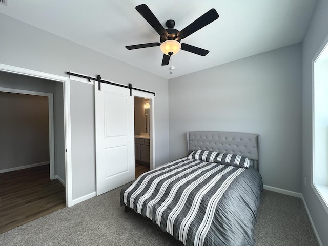 bedroom featuring ensuite bath, ceiling fan, a barn door, and dark colored carpet