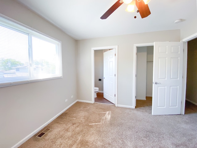 unfurnished bedroom featuring a walk in closet, ensuite bath, a closet, ceiling fan, and light colored carpet