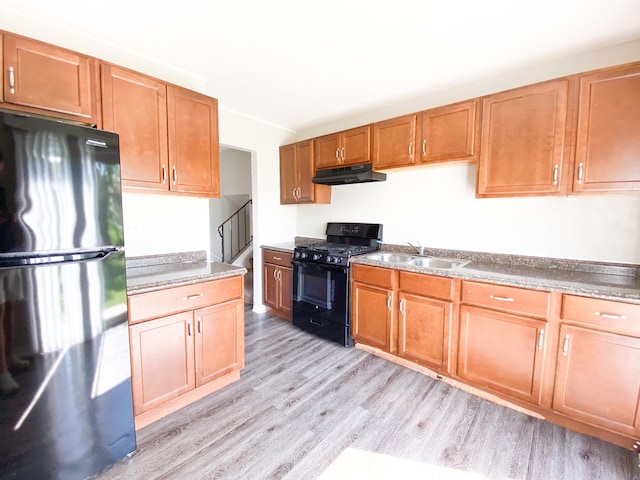 kitchen with black gas range oven, sink, light hardwood / wood-style flooring, and stainless steel fridge