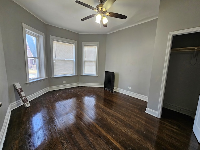 unfurnished bedroom featuring dark hardwood / wood-style flooring, ceiling fan, radiator heating unit, and a closet