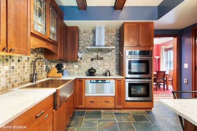 kitchen featuring stainless steel double oven, backsplash, dark tile floors, and wall chimney exhaust hood