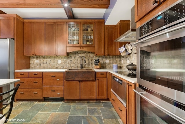 kitchen featuring wall chimney range hood, dark tile floors, stainless steel appliances, tasteful backsplash, and sink