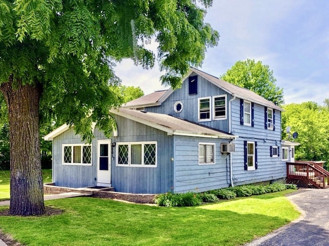 view of front of home with a wall unit AC and a front lawn