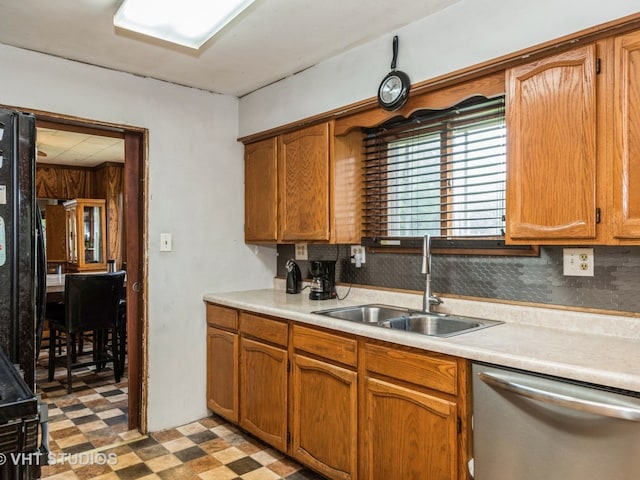 kitchen featuring brown cabinetry, dark floors, light countertops, stainless steel dishwasher, and a sink