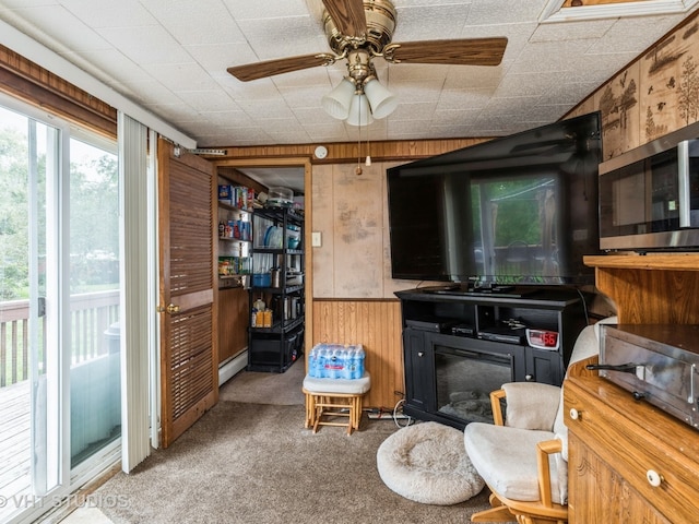 interior space with wood walls, a baseboard radiator, carpet flooring, and a ceiling fan