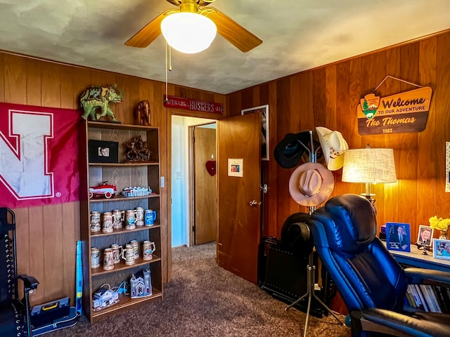 home office with ceiling fan, wooden walls, and dark colored carpet