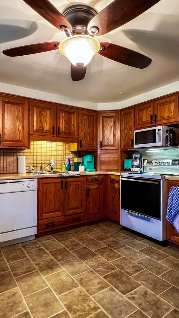 kitchen with dark tile floors, white appliances, backsplash, sink, and ceiling fan