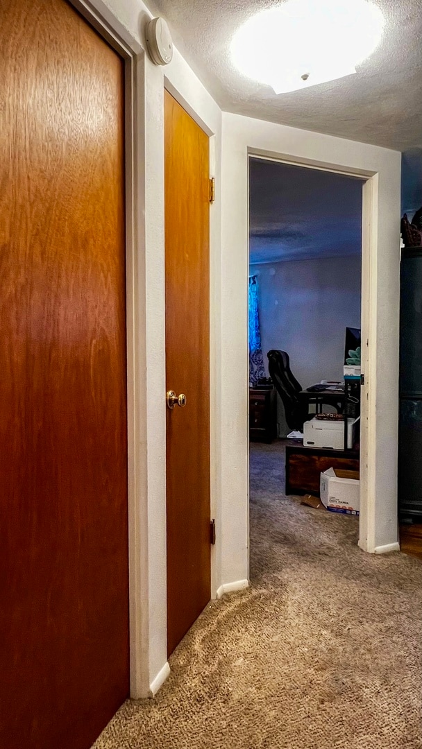 hallway featuring a textured ceiling and dark carpet