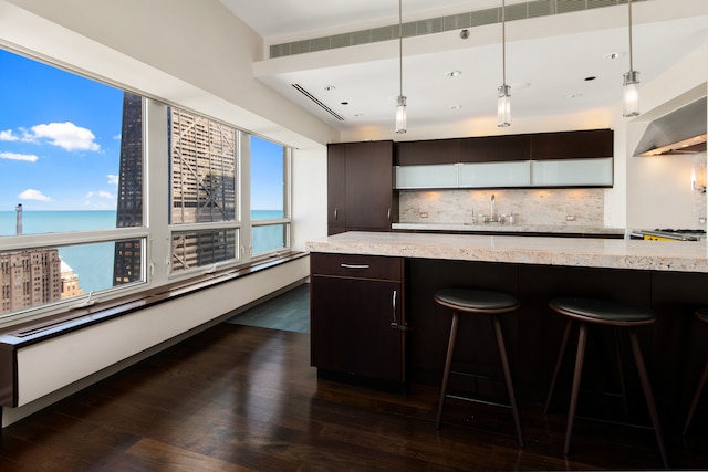 kitchen featuring dark wood-type flooring, a kitchen breakfast bar, wall chimney range hood, tasteful backsplash, and pendant lighting