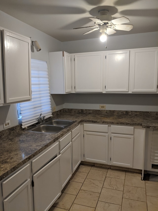 kitchen featuring ceiling fan, light tile floors, dark stone counters, sink, and white cabinets