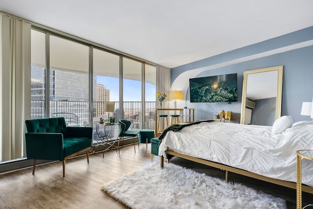 bedroom featuring floor to ceiling windows, a wall mounted AC, access to exterior, and hardwood / wood-style flooring