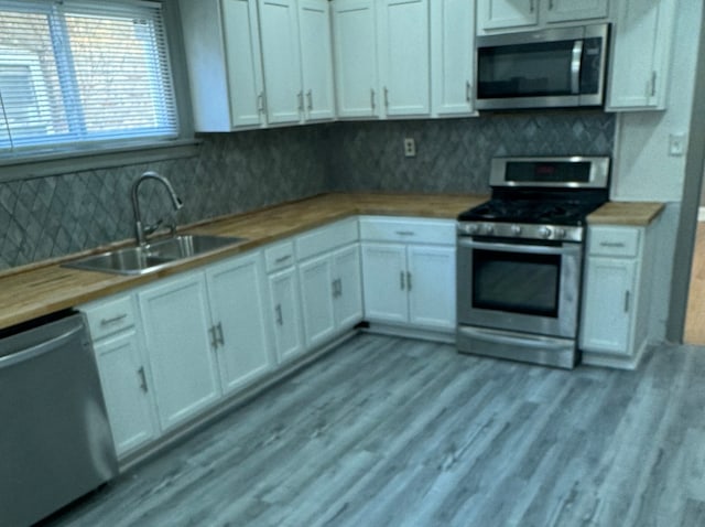 kitchen with tasteful backsplash, white cabinets, stainless steel appliances, light hardwood / wood-style flooring, and sink