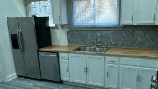 kitchen with white cabinetry, light hardwood / wood-style floors, sink, stainless steel appliances, and tasteful backsplash