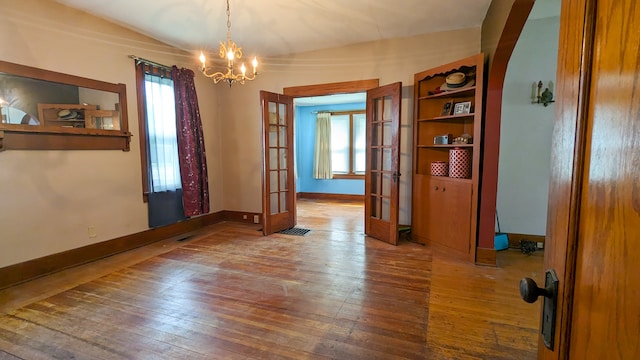 empty room featuring plenty of natural light, french doors, wood-type flooring, and an inviting chandelier