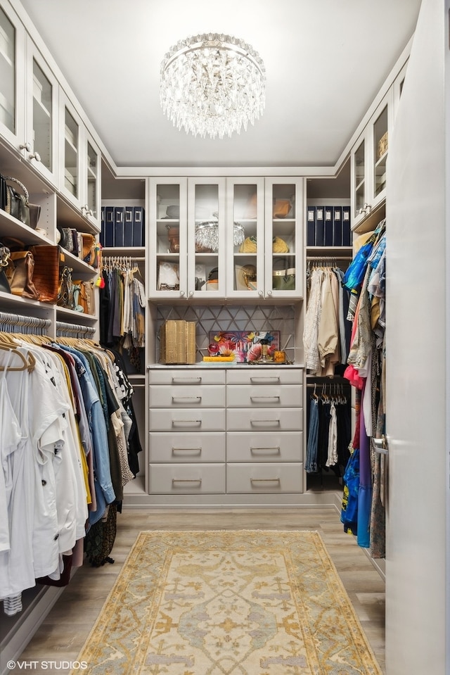 spacious closet featuring light hardwood / wood-style floors and an inviting chandelier