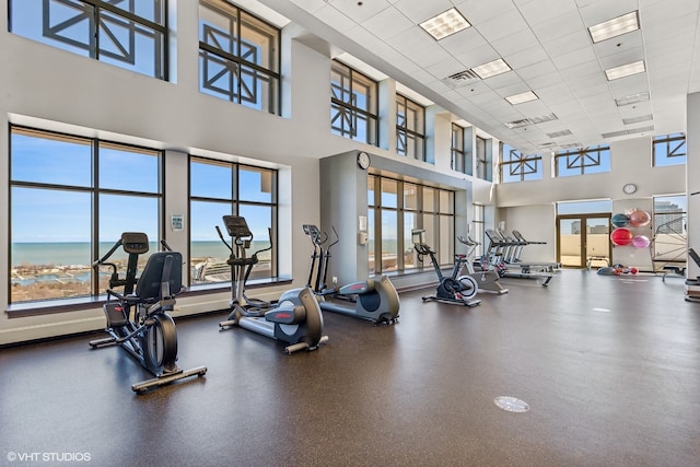 gym featuring a towering ceiling, a paneled ceiling, and a water view