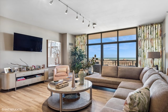 living room with rail lighting, a water view, light wood-type flooring, and floor to ceiling windows