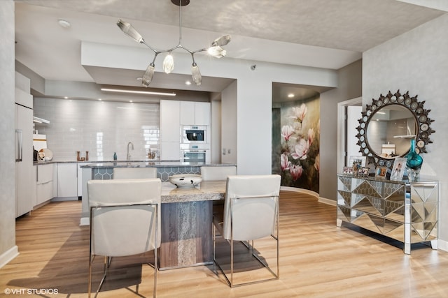 kitchen featuring a kitchen breakfast bar, light hardwood / wood-style flooring, hanging light fixtures, backsplash, and white cabinets