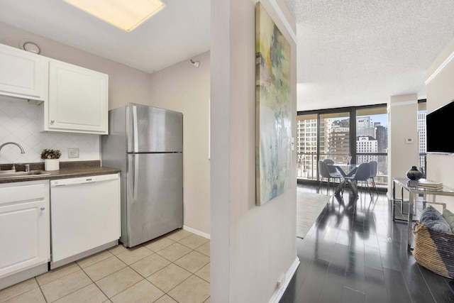 kitchen with stainless steel fridge, floor to ceiling windows, white dishwasher, sink, and white cabinetry