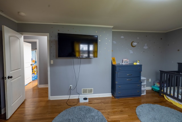 bedroom with ornamental molding, wood-type flooring, and a crib