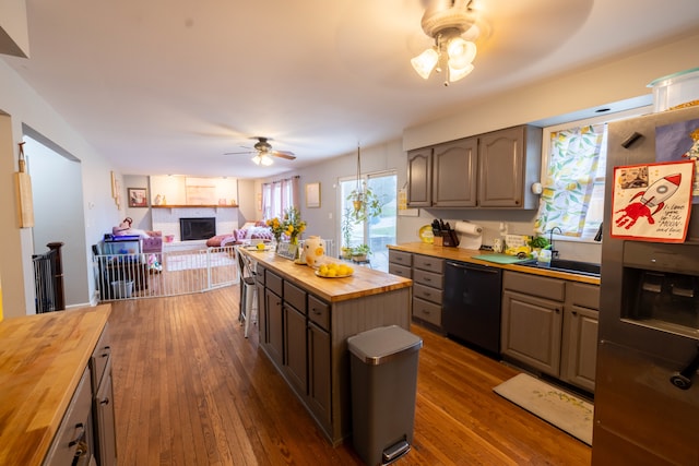 kitchen featuring dishwasher, a brick fireplace, ceiling fan, butcher block counters, and dark hardwood / wood-style floors