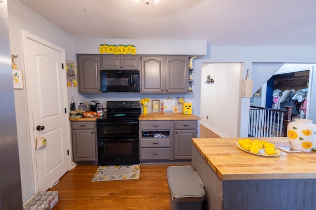 kitchen featuring dark wood-type flooring, gray cabinets, butcher block counters, and black appliances