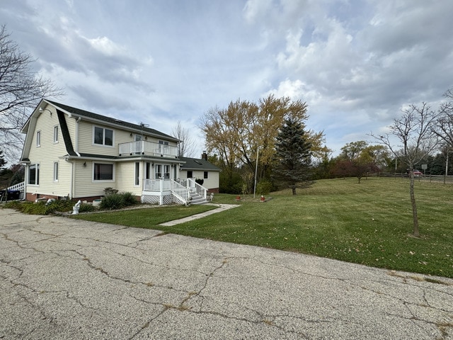 view of front facade with a gambrel roof, a front yard, and a balcony