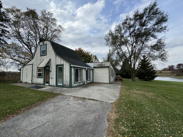 exterior space featuring aphalt driveway, a lawn, a gambrel roof, a garage, and an outdoor structure