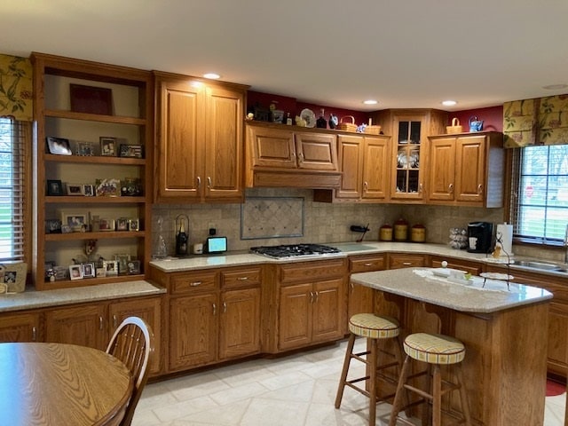 kitchen with light tile floors, light stone counters, a kitchen breakfast bar, backsplash, and a center island