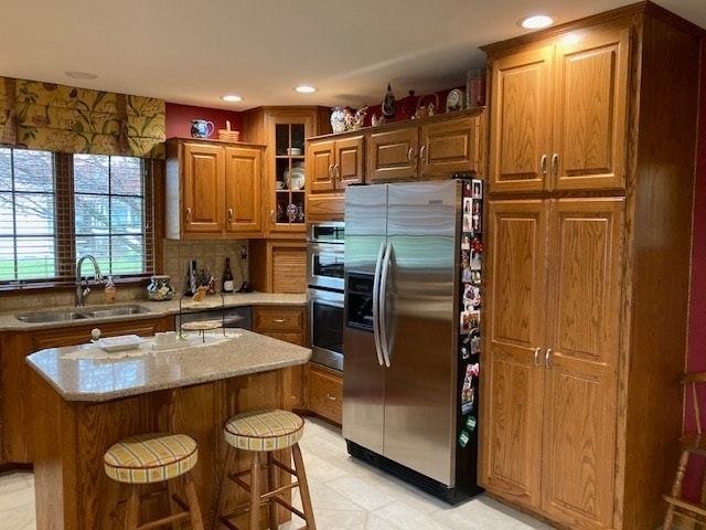 kitchen featuring sink, a breakfast bar, stainless steel appliances, light stone countertops, and a center island