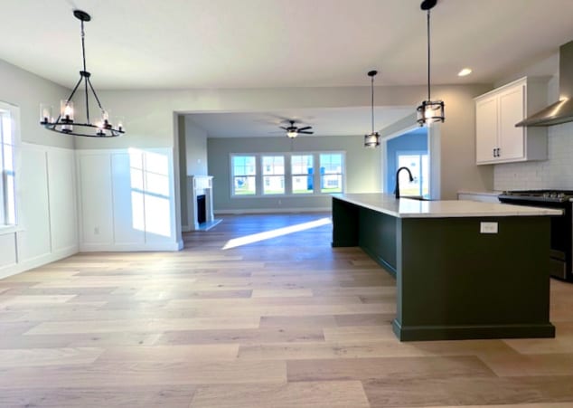 kitchen with range, backsplash, a kitchen island with sink, white cabinets, and pendant lighting