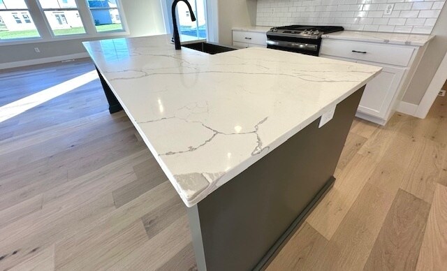 kitchen featuring stainless steel gas stove, tasteful backsplash, an island with sink, light hardwood / wood-style floors, and white cabinets