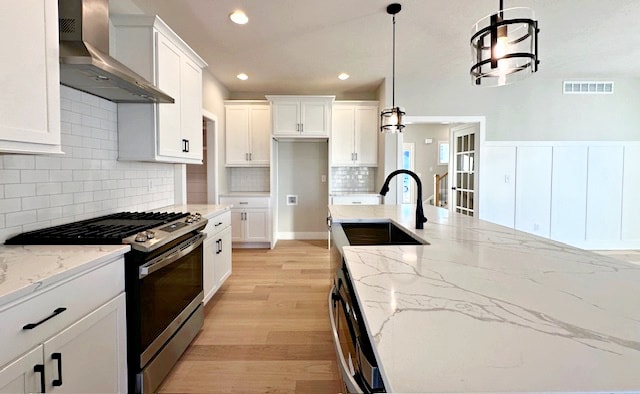 kitchen with light hardwood / wood-style flooring, wall chimney range hood, white cabinets, and stainless steel gas range oven